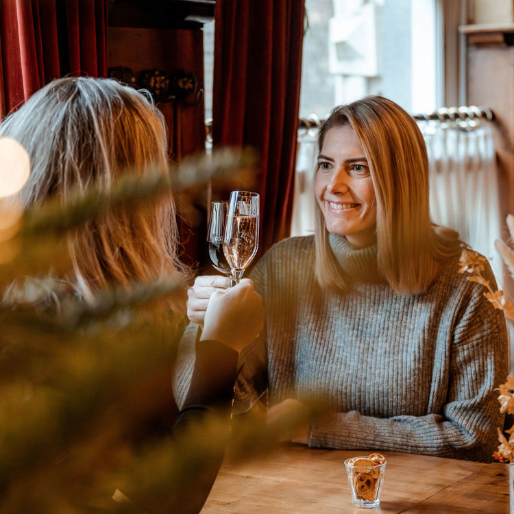 Twee vriendinnen proosten met glas champagne in een knus cafe tijdens de kerstperiode. 