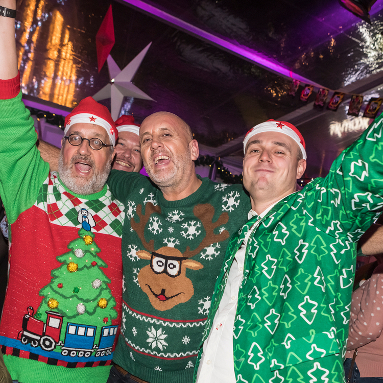 Drie mannen in kerstkleding naast elkaar met armen in de lucht