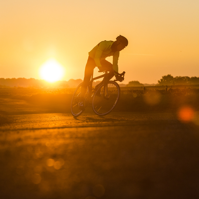 Wielrenner met ondergaande zon op de achtergrond. 