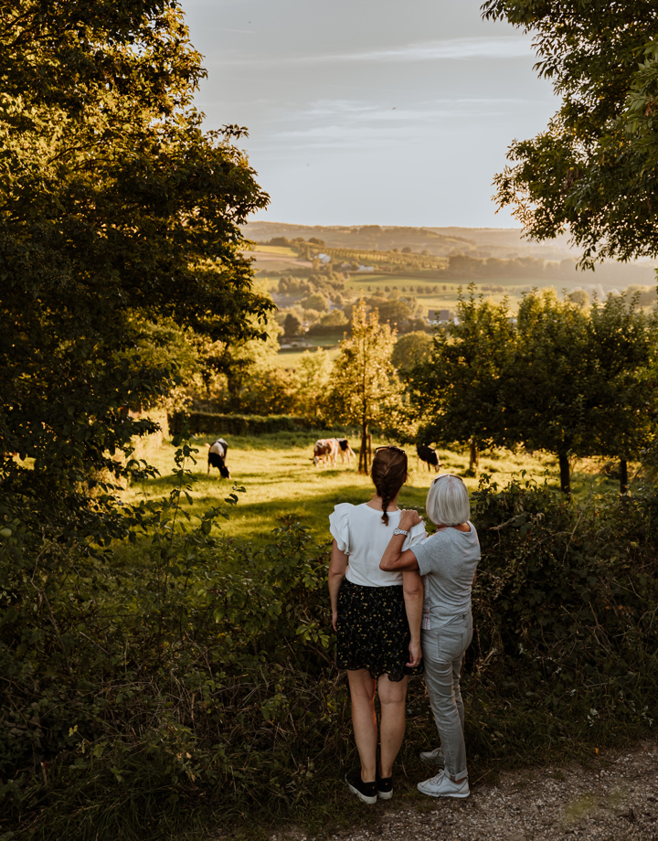 Moeder en dochter kijken uit over een weiland met koeien en het uitzicht daarachter 