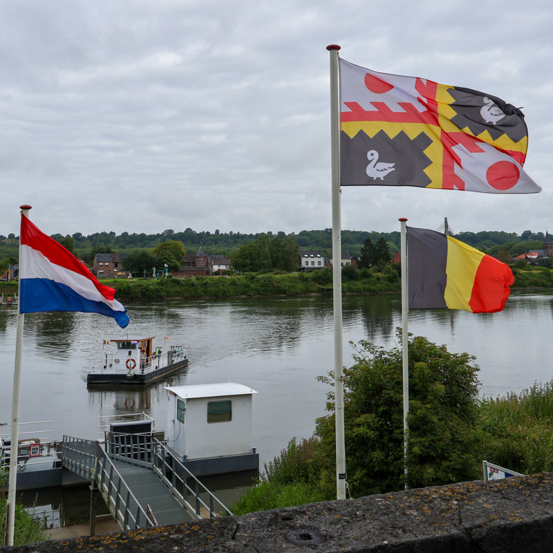 Veerpondje steekt over de Maas in Eijsden met wapperende vlaggen aan de kade. 