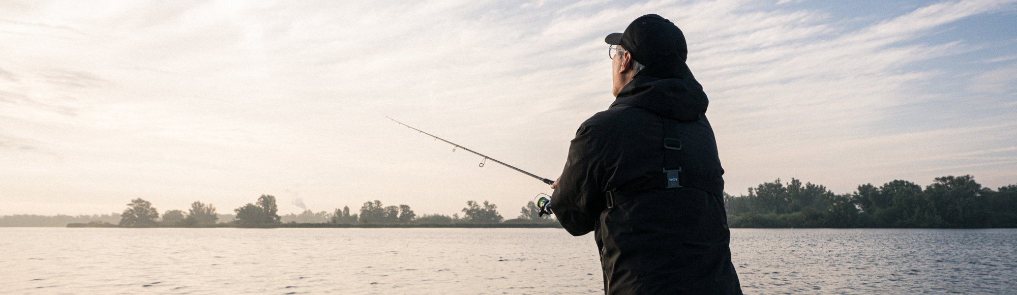 Visser gooit vanaf een vissersbootje een hengel uit in het water.