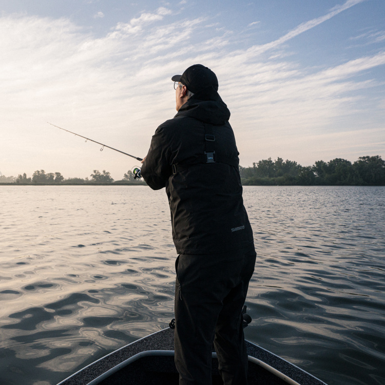 Visser gooit vanaf een vissersbootje een hengel uit in het water.