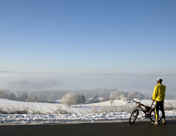 Persoon naast fiets uitkijkend over besneeuwd heuvellandschap