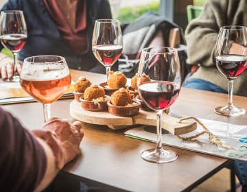 Close up van bitterballen met daarop een toefje van een wit sausje te midden van glazen rode wijn en speciaal bier