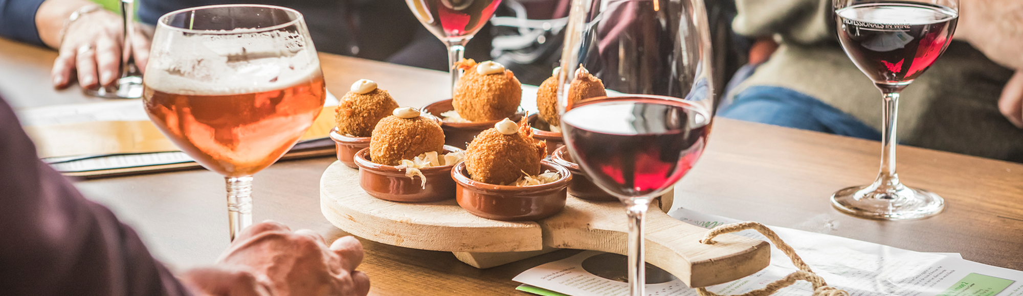 Close up van bitterballen met daarop een toefje van een wit sausje te midden van glazen rode wijn en speciaal bier