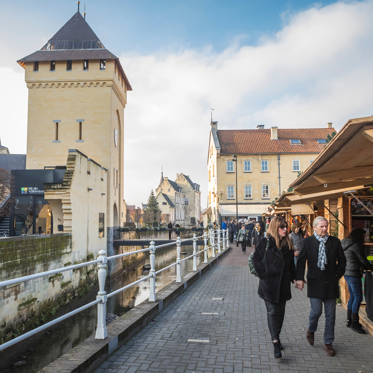 Mensen lopen langs kerstkraampjes op Santa's Village met op de achtergrond de Geultoren.
