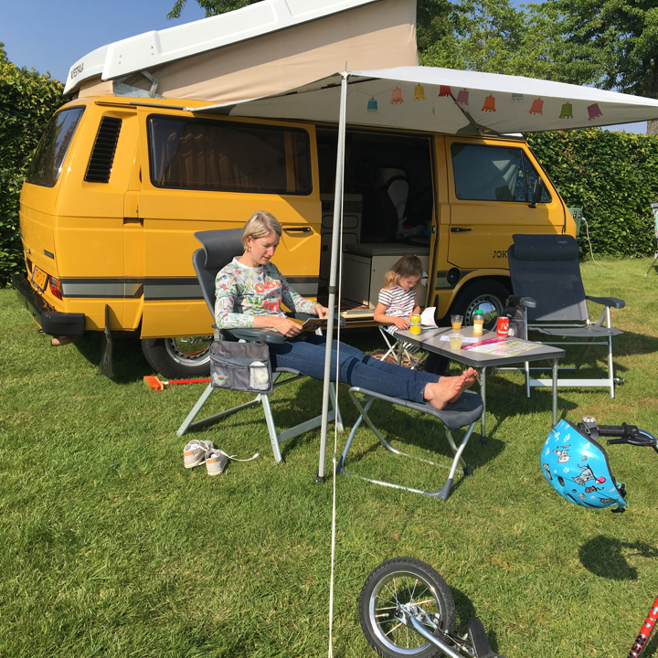 Moeder en dochter zitten in een stoel voor het camperbusje op de camping. 