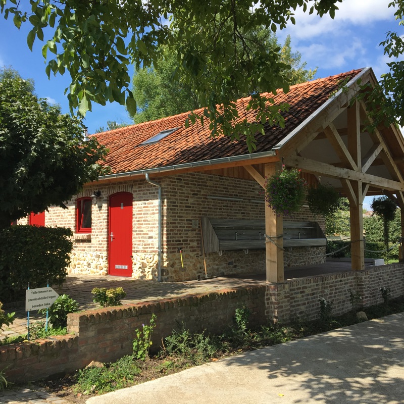 Sanitairgebouw van mergelsteen met een rode deur. 