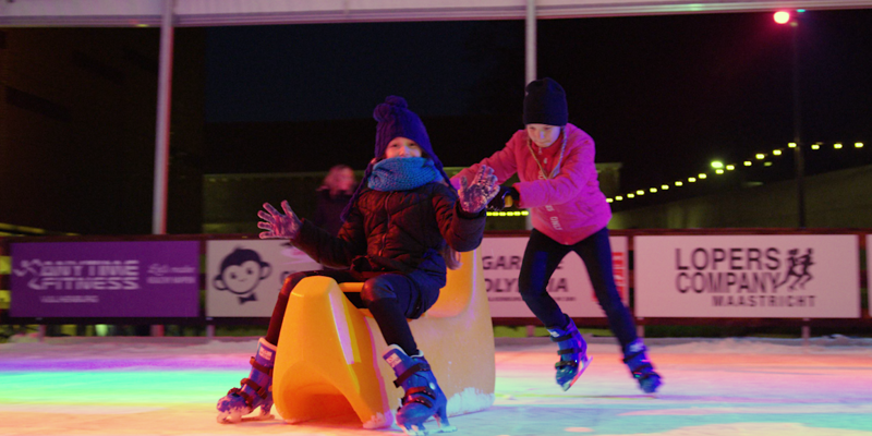 kind duwt al schaatsend kind vooruit op oranje plastic schaatshulpmiddel
