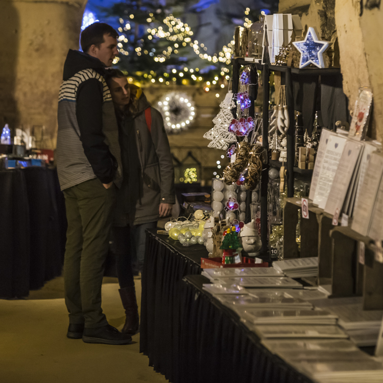 Jonge vrouw heeft hoofd op schouder van jongeman terwijl ze kijken naar kerstartikelen in kerstmarkt Fluweelengrot