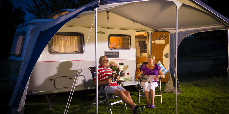 Echtpaar zit in de avond op twee stoelen voor de caravan. 