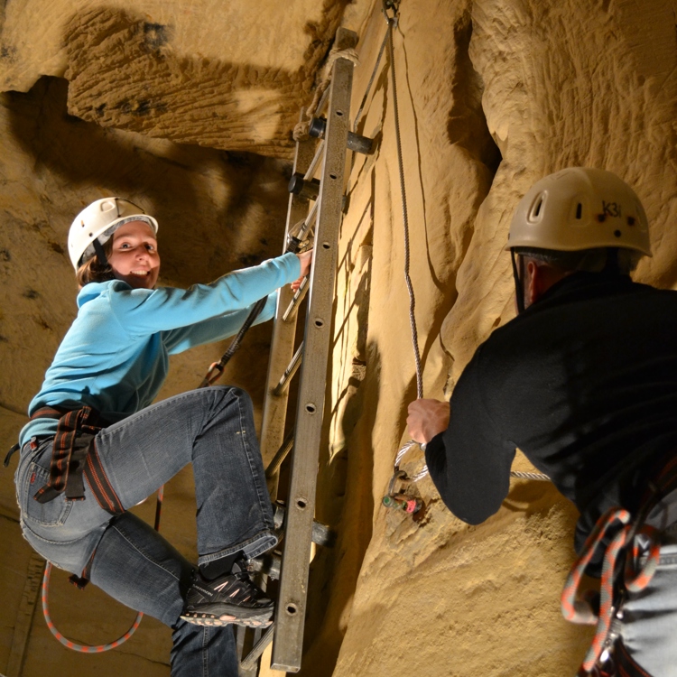 Twee personen ondernemen een survivaltocht door een mergelgrot. Een staat op een ladder, de ander houdt de lijn vast