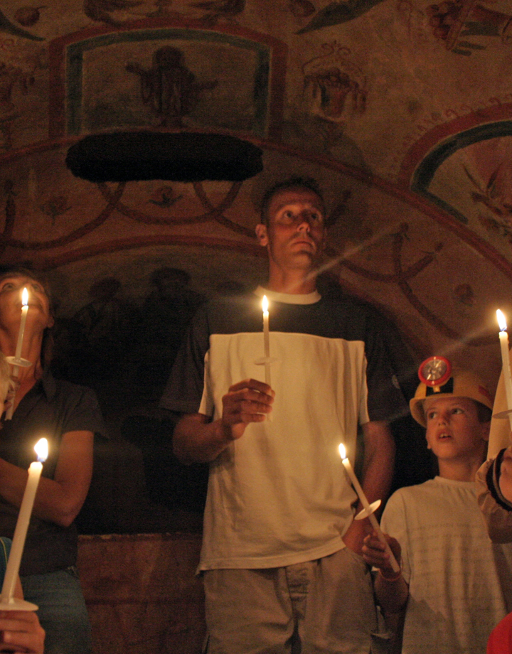 Mensen en kinderen die ieder een kaars vasthouden in de Romeinse Katakomben van Valkenburg