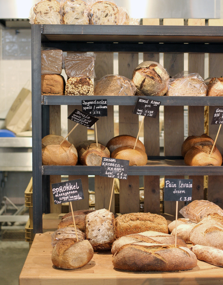 Rek met verschillende broden en daarin prikkers met productnamen op kleine krijtbordjes