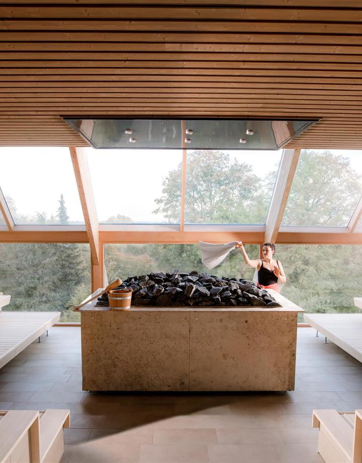 Vrouwelijke saunameester zwaait met doek in lege panoramasauna van Thermae 2000