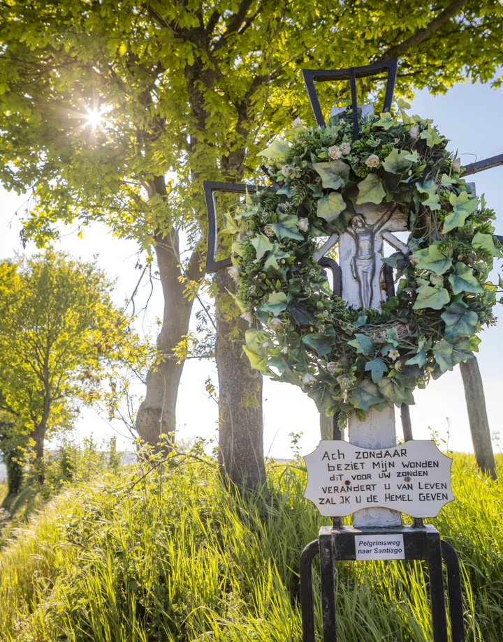 Wegkruis met krans van klimop naast veldweg en bomen