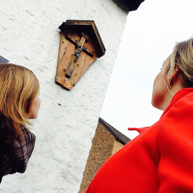 Jenneke en Leonie voor een wegkruis aan een wit gebouw
