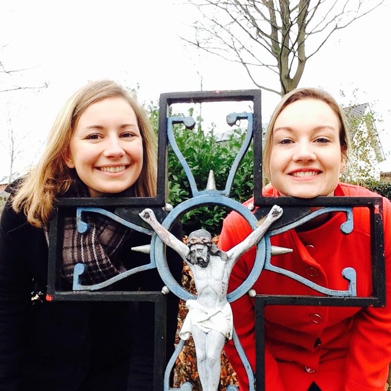 Jenneke en Leonie met voorovergebogen hoofden achter een wegkruis