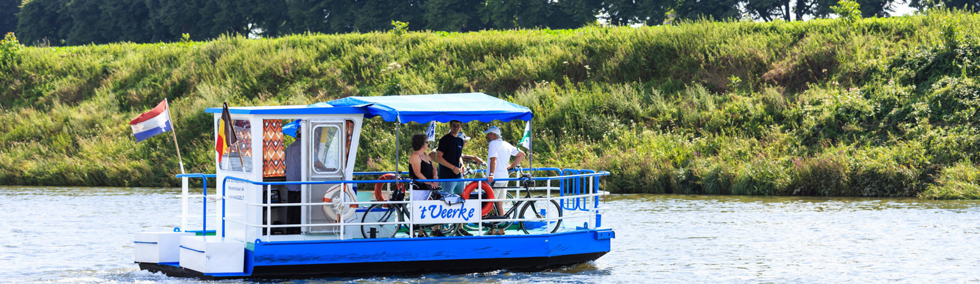 Het veerpontje met fietsers steekt de Maas over van Nederland naar België