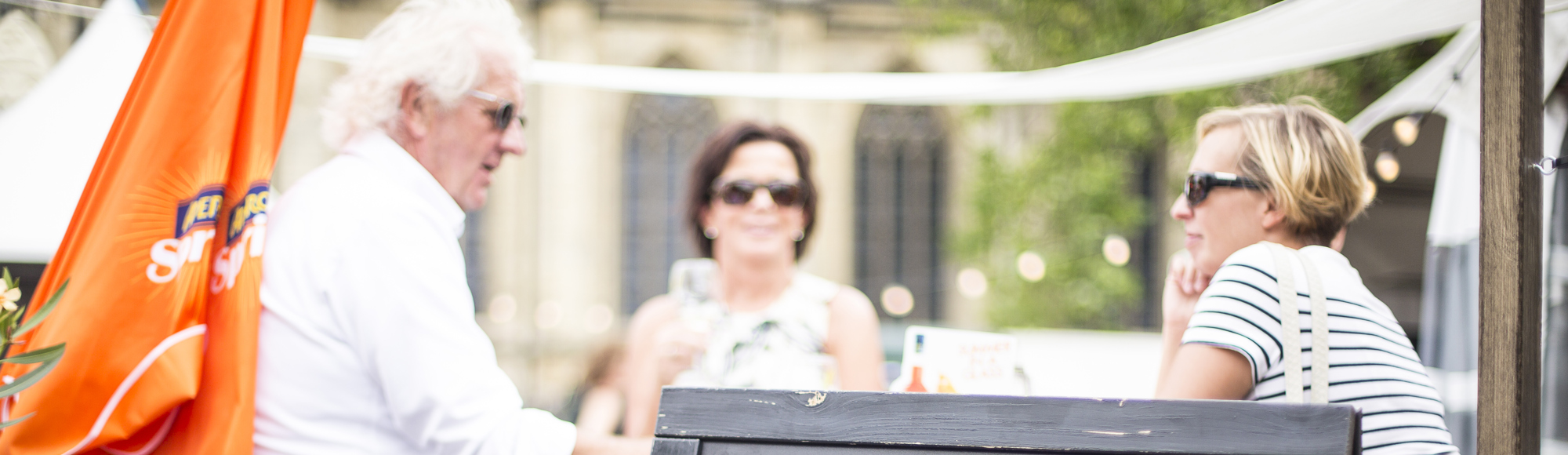 Twee vrouwen en een man zitten aan een hoge tafel achter een bord met het kaasplank menu
