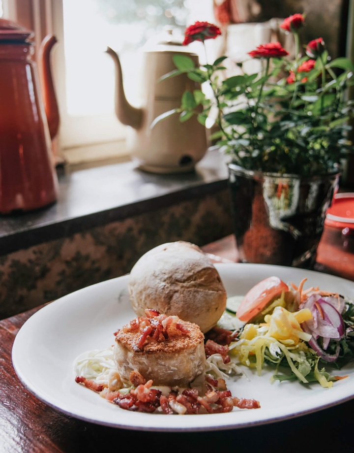 Een close up van een kippenpasteitje met spekjes, een broodje en garnering in een gezellige herberg
