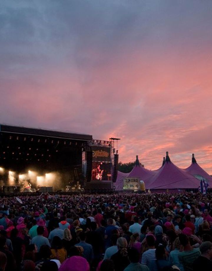 Publiek en podium met daarnaast roze tenten op Pinkpopterrein met rozig schemerlicht