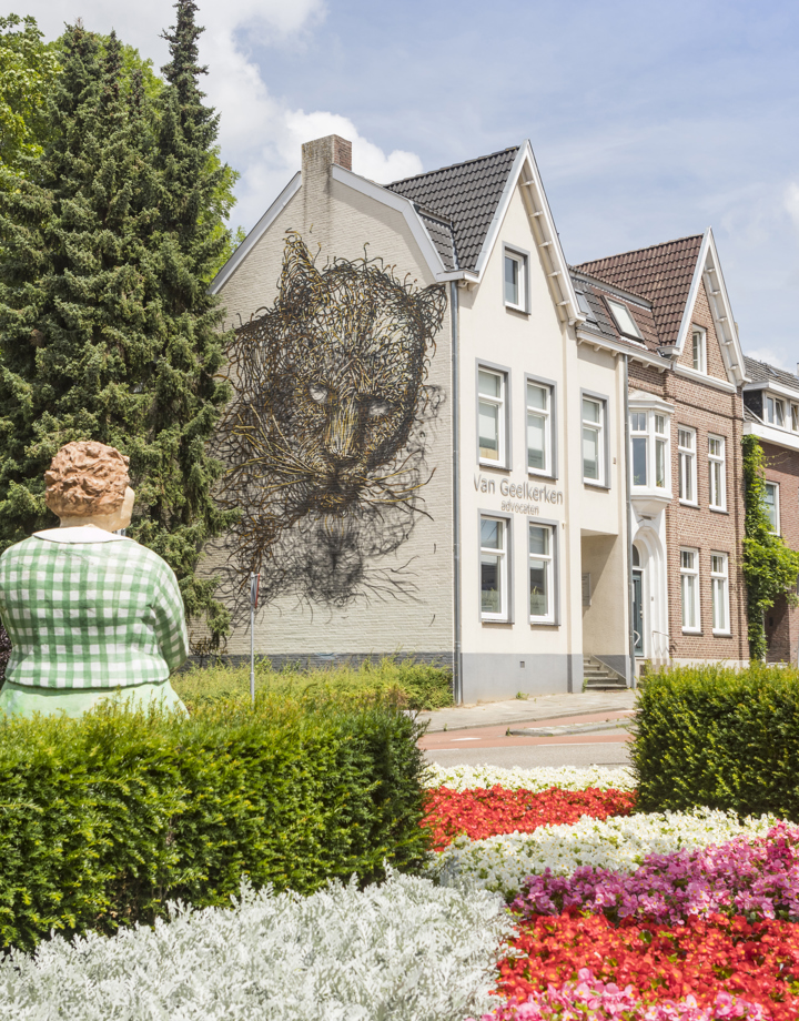 Een sculptuur van een alledaagse vrouw kijkt naar een grote mural van een zwarte katachtige op een gevel in Heerlen