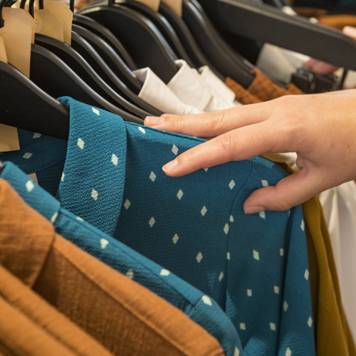 Een hand die kleding bekijkt in een kledingrek