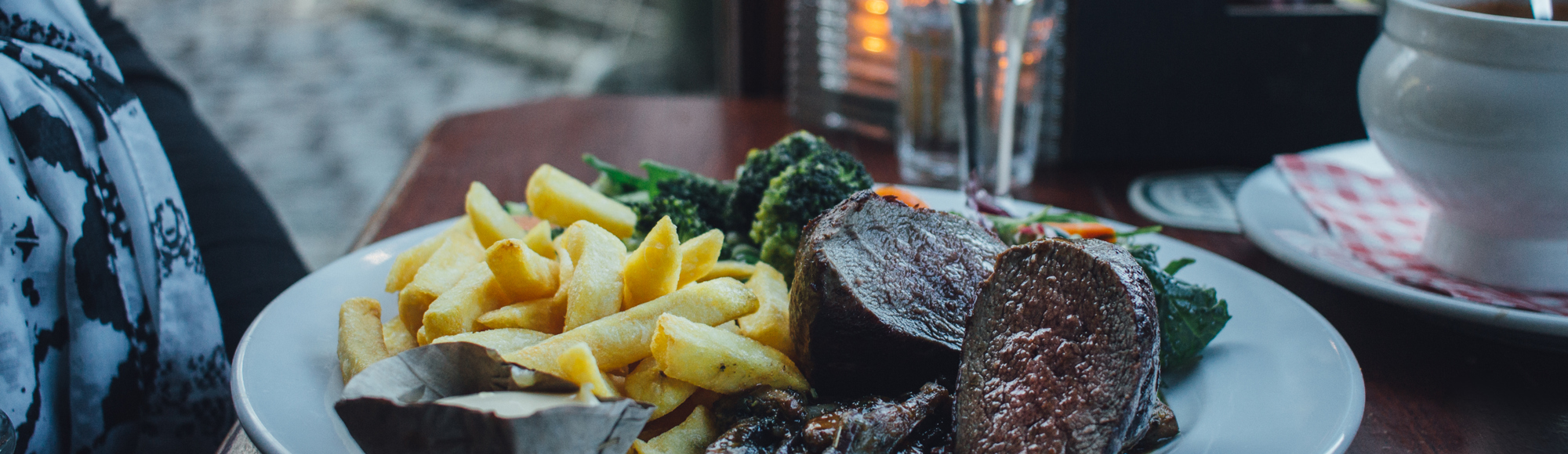 Een knus gedekt tafeltje met een bord vol friet, wild, en groenten, een uiensoep en een biertje