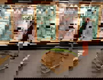 Meneer in tentoonstelling met urnen en informatiezuilen over grafstenen