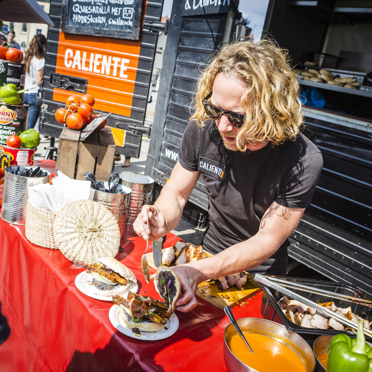 Een man met blond haar vult een culinair broodje met vlees