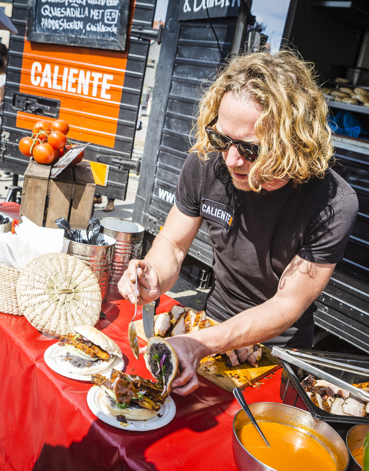 Een man met blond haar vult een culinair broodje met vlees
