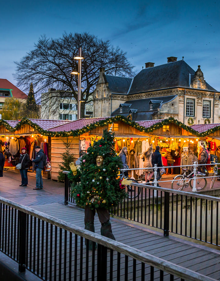 Man in kerstboompak op brug voor kerstkraampjes