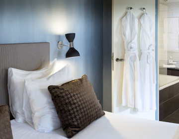 luxe hotelkamer met een stukje van het hotelbed, twee badjassen en een kijkje in de badkamer. 