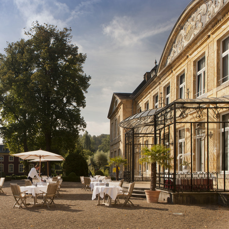 Ober staat bij een tafel bij het terras van Chateau St. Gerlach op een zonnige dag