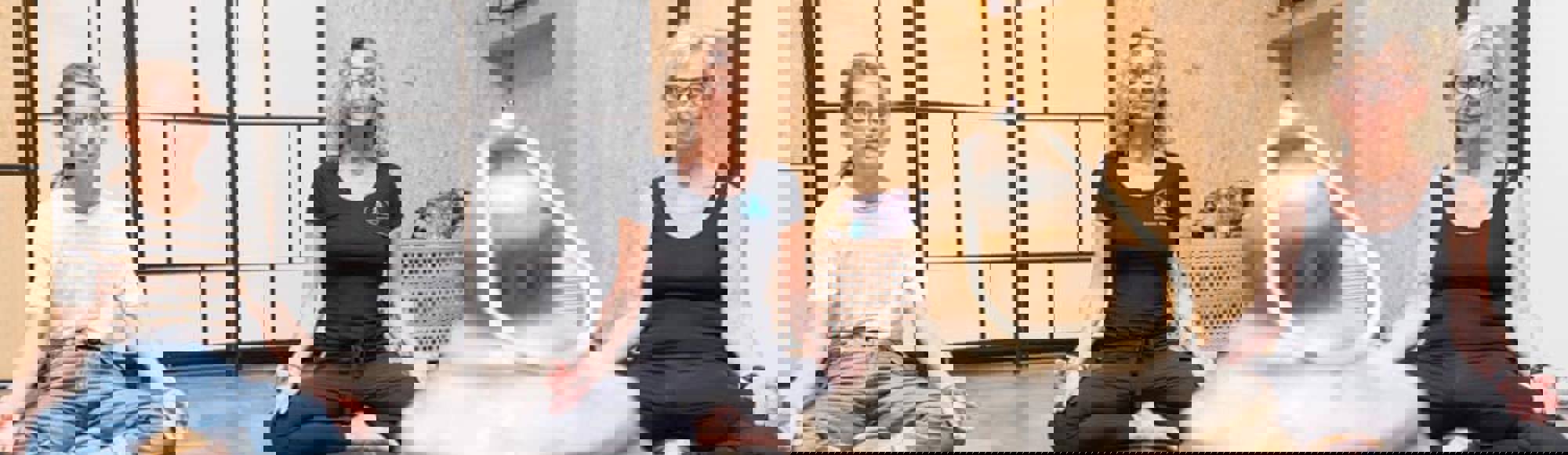 Drie dames zitten met ogen gesloten in yoga houding op een yoga mat