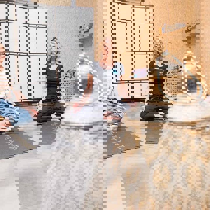 Drie dames zitten met ogen gesloten in yoga houding op een yoga mat