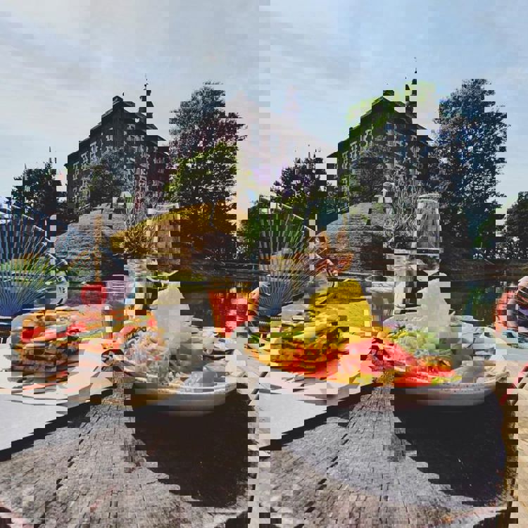 Lunchgerechten en drankjes op een houten tafel met uitzicht op Kasteel Limbricht