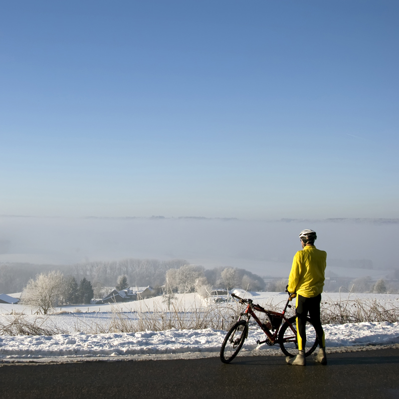Een MTB'er kijkt uit over een besneeuwd landschap terwijl hij naast zijn fiets staat