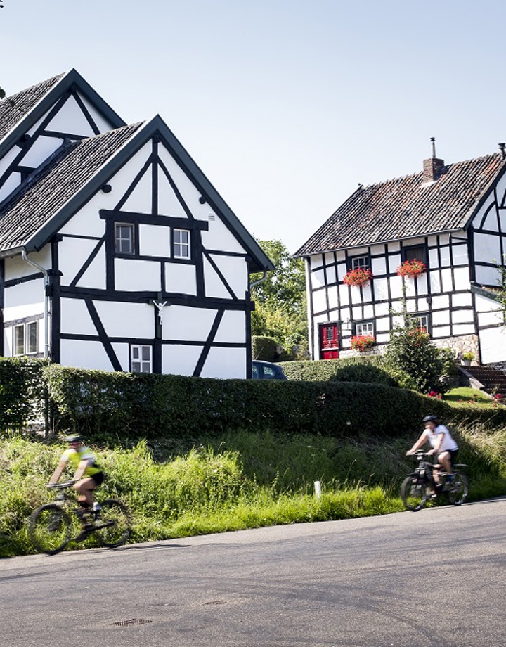 Twee sportieve fietsers dalen een weg af langs twee vakwerkhuizen