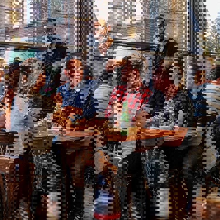 Een ober praat met een vijftal gasten aan een tafeltje aan het raam