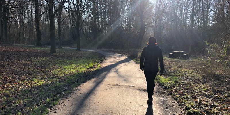 Een vrouw wandelt over een verharde weg door het bos