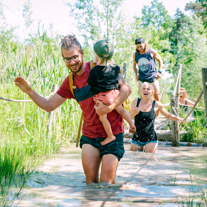 Vader tilt dochtertje over een diepe waterplas bij het blotevoetenpad