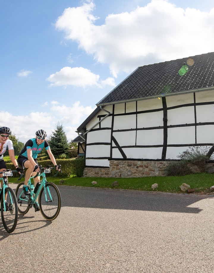 Een groepje wielrenners fietst langs een vakwerkwoning