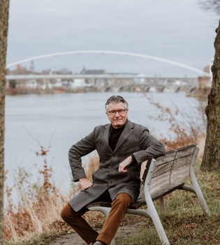 Camille Oostwegel zit op een bankje langs de Maas voor de voetgangersbrug
