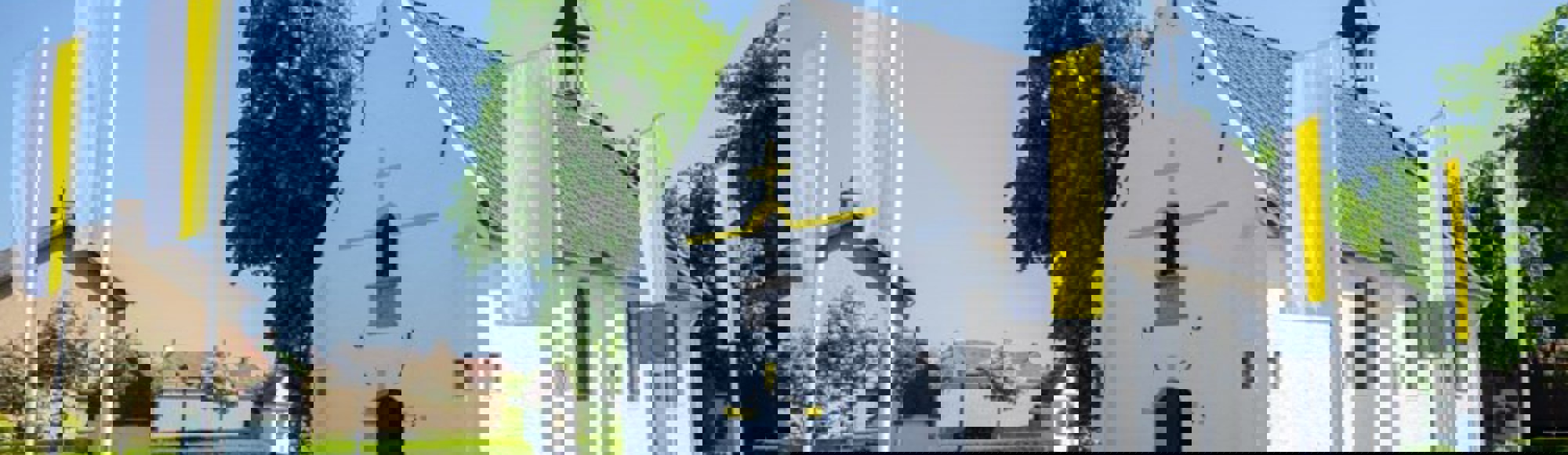 Een witte kapel gelegen aan een straat omringd met witgele vlaggen