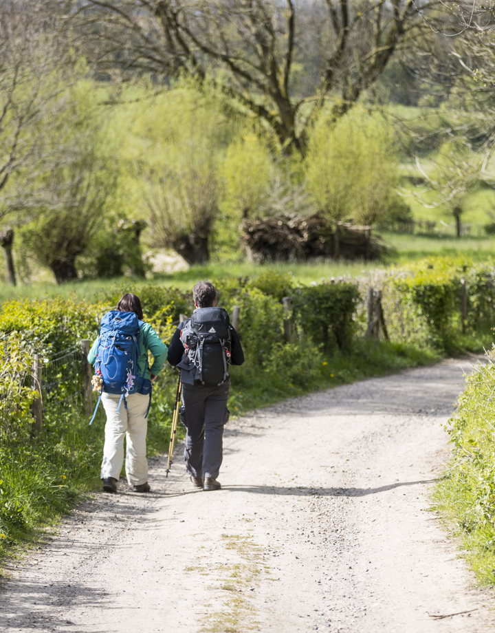 Twee dames met backpack wandelen over een onverharde weg richting de heuvels