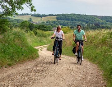 Een man en een vrouw op een fietst beklimmen een verharde weg in het heuvelland
