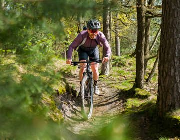 Een mountainbiker fietst lachend over een smal paadje in een zonnig bos